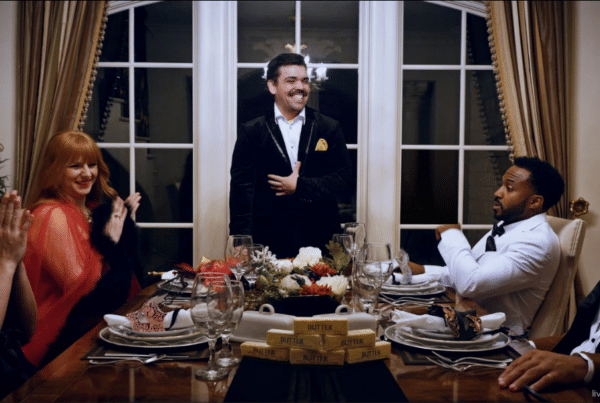 Cybersecurity training. A smiling man stands at the head of a table with two women and two men seated on each side. All are dressed for a masquerade ball.