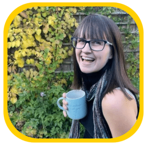 Abbie Horning - head of communications - a woman with darrk hair and a fringe smiling in a garden with a blue mug and a colourful scarf